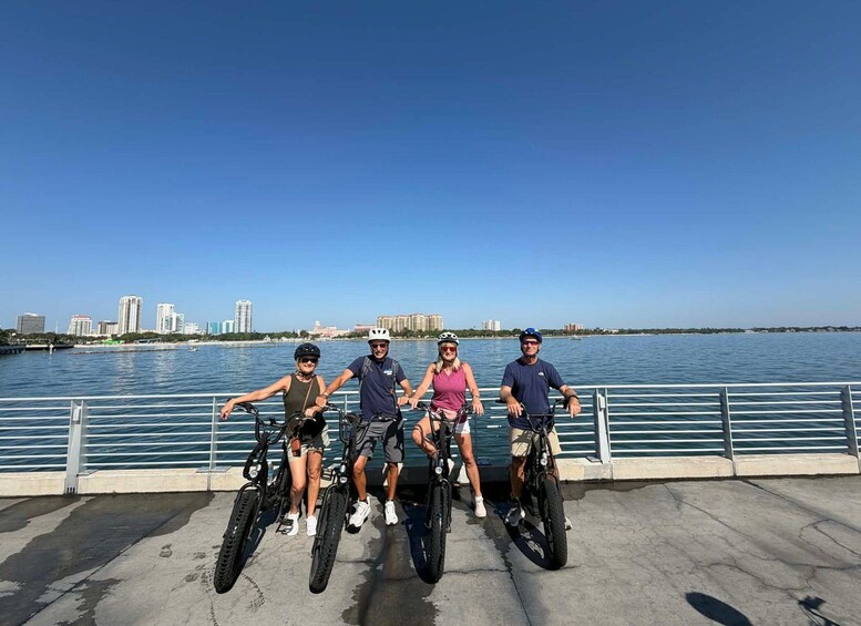 Four people on bicycles by a waterfront with a city skyline in the background. 5