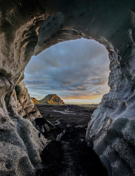 Una cueva de hielo con vista a una montaña y un cielo nublado. 2