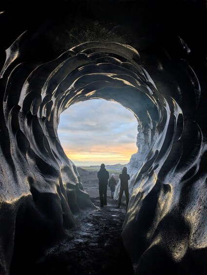 A tunnel with a natural archway, people walking through, and a sunset in the background. 5