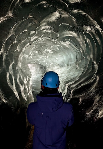 A person in a blue helmet and jacket observing an ice cave. 3