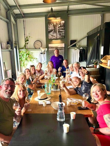 A group of people sitting around a wooden table in a rustic indoor setting, holding glasses of wine. 5