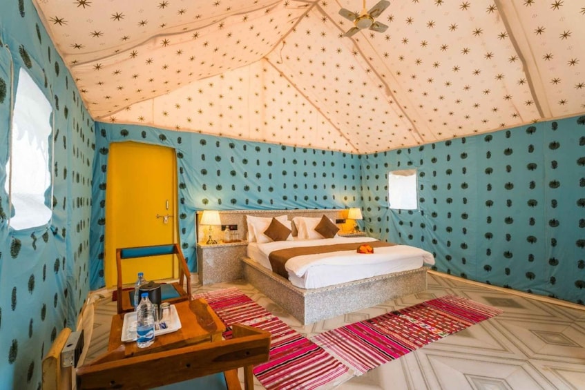 A tented room with a bed, a table with a bottle, and patterned walls. 4