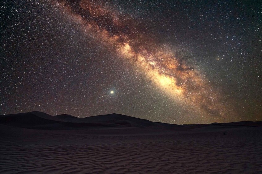 A starry night sky over a desert landscape with sand dunes. 3