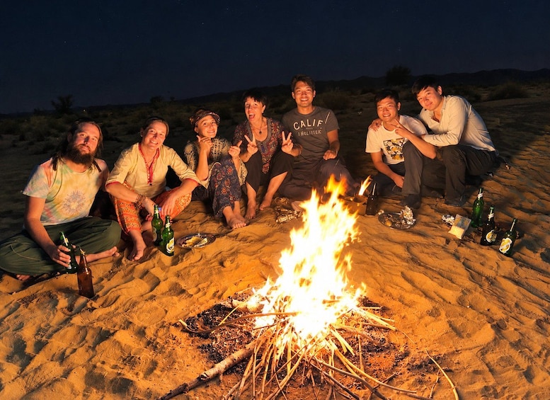 A group of people sitting around a campfire on a sandy beach at night. 2