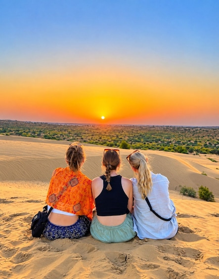Three people sitting on sand dunes during sunset. 5