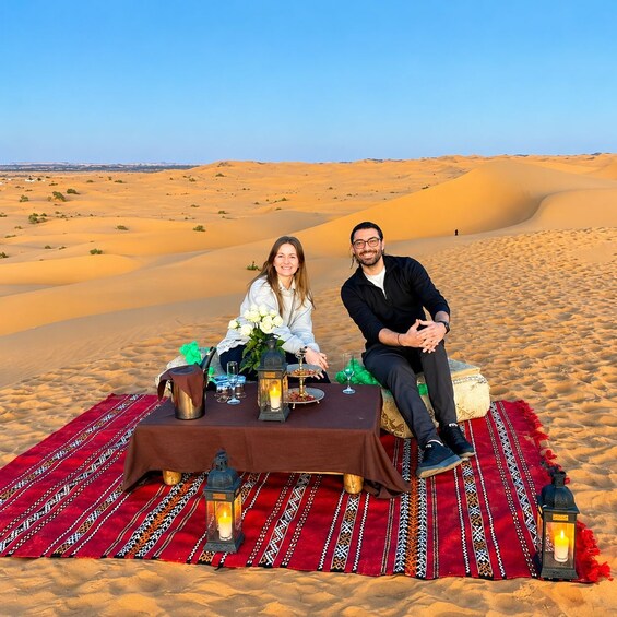 A couple sitting on a blanket in a desert with sand dunes in the background. 4