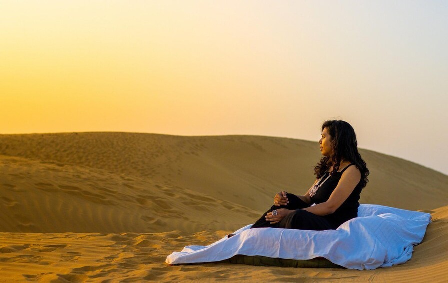 A person sitting on a sand dune during sunset. 4
