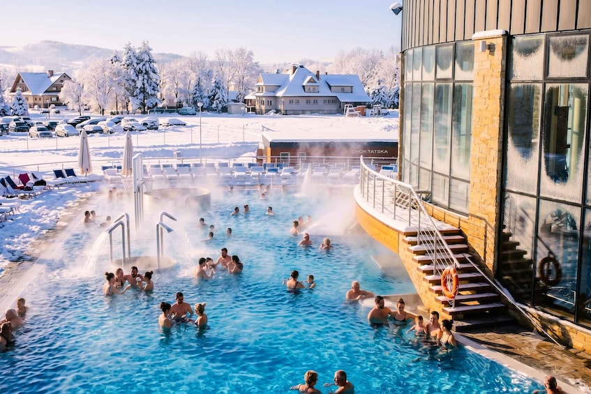A hot spring with people swimming and relaxing, surrounded by snow-covered trees and buildings. 3