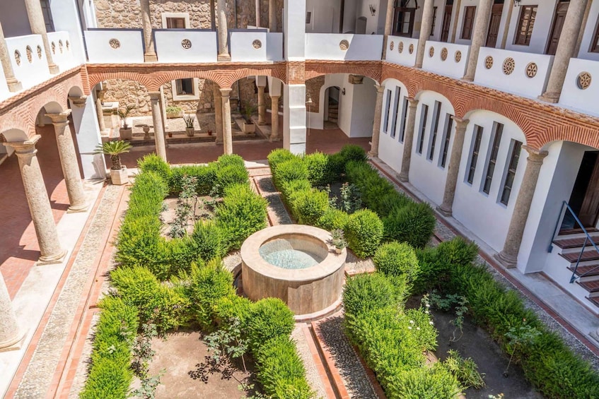 A courtyard with a central fountain, surrounded by neatly trimmed hedges and stone columns. 1