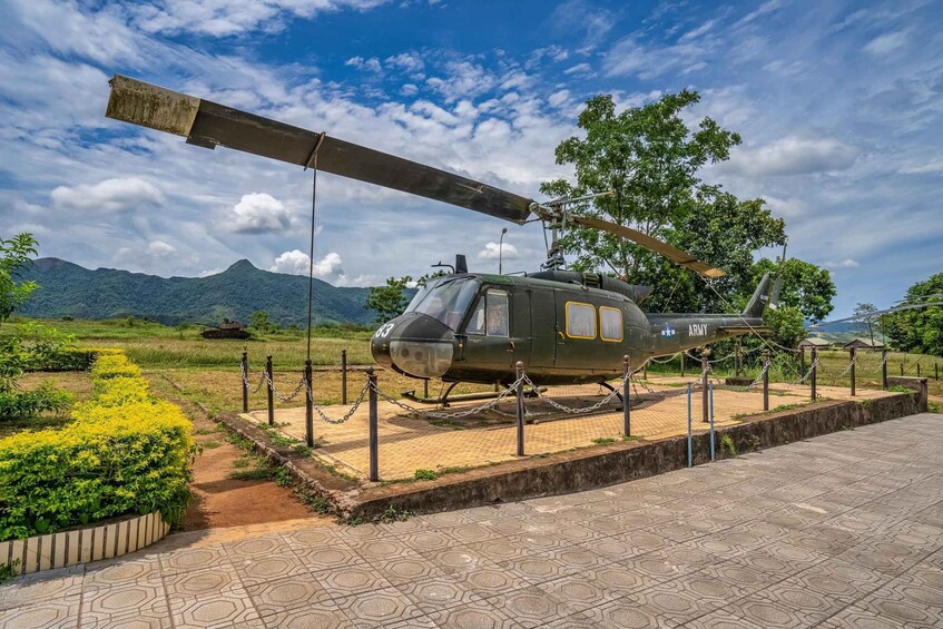A military helicopter on display, surrounded by a chain-link fence, with a mountainous landscape in the background. 4