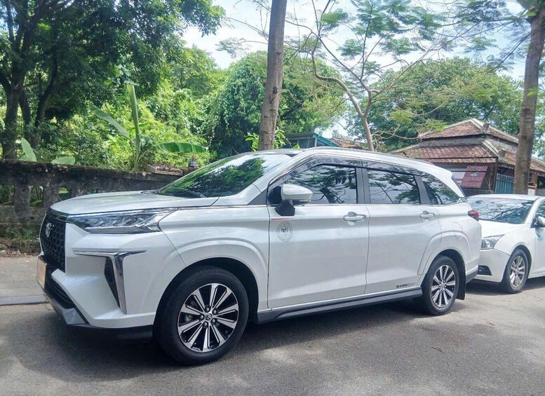 A white SUV parked on a street with trees and a building in the background. 2