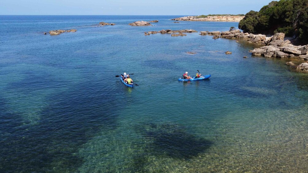 Two people kayaking on a calm sea with clear water and rocky outcrops in the background. 2