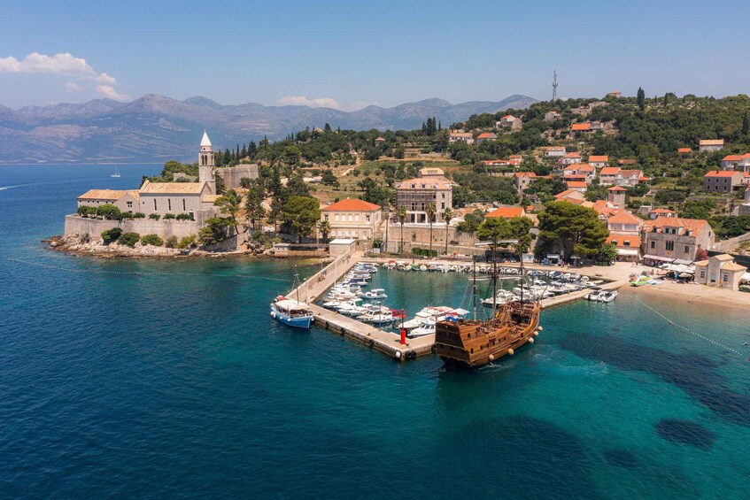 A coastal town with a historic church, a marina with boats, and a mountainous backdrop. 3