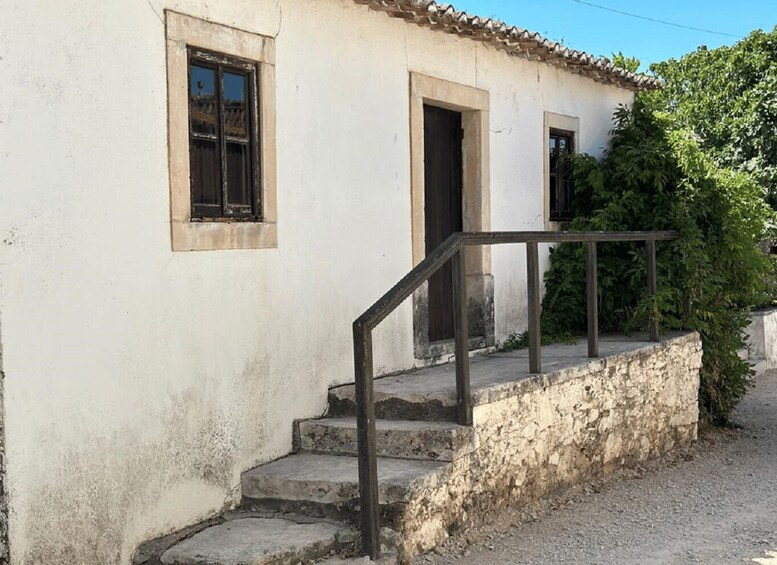 A white building with a tiled roof, a set of stone steps, and a metal railing. 2