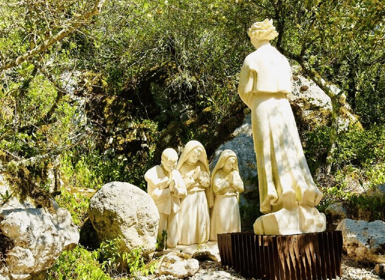 A statue of a woman and children in a natural setting with rocks and greenery. 3