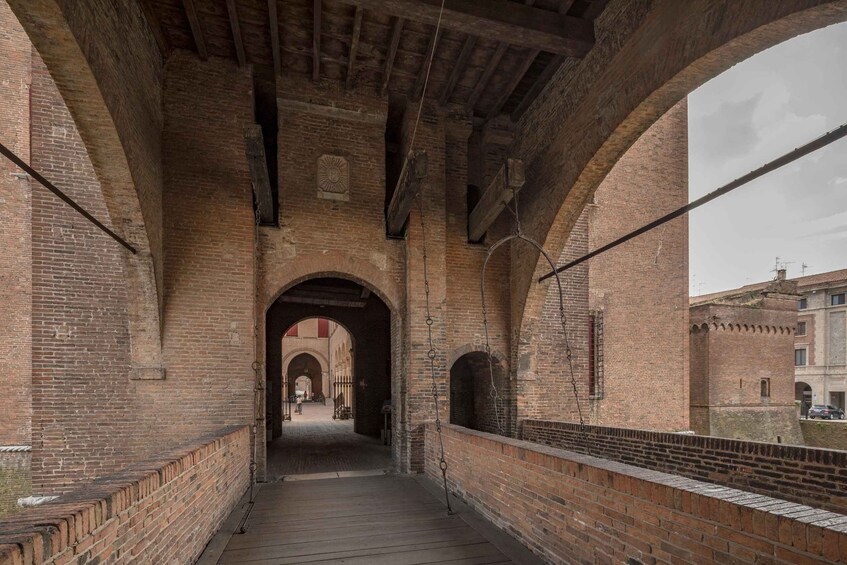An arched brick corridor with wooden flooring and a metal railing on one side. 2