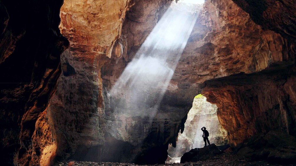 A cave with a waterfall and a person standing on a rock. 1