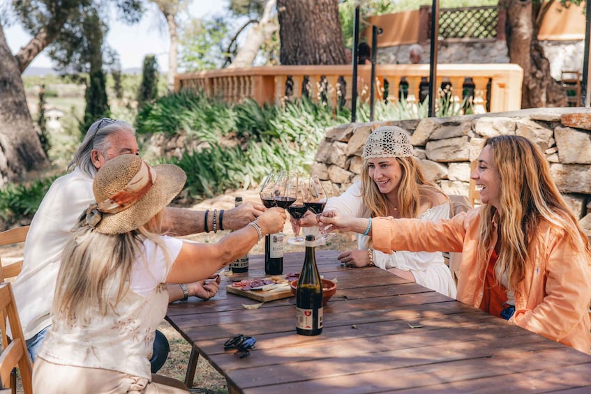 A group of people toasting with wine at an outdoor table with a stone wall and greenery in the background. 1