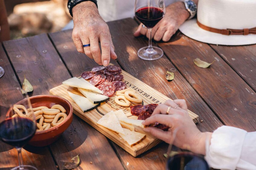 A wooden table with a charcuterie board, wine glasses, and a bowl of pretzels. 2