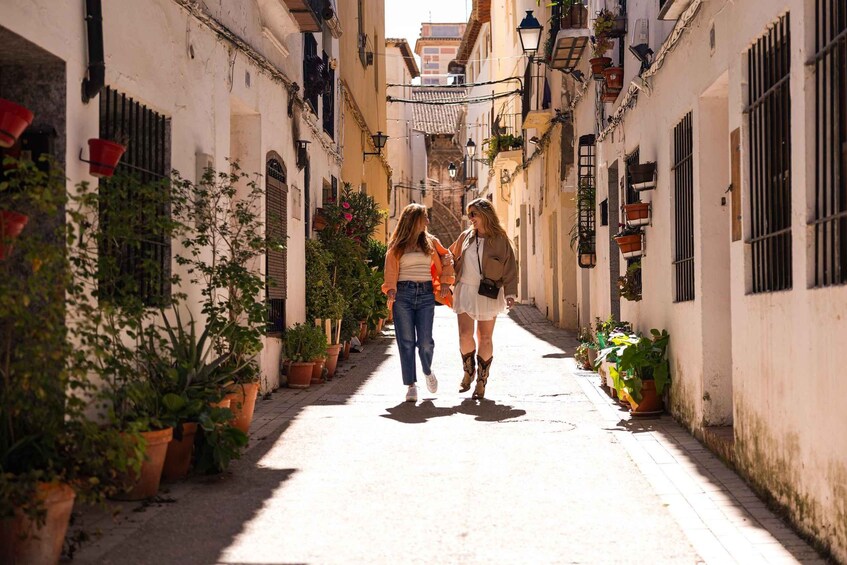A narrow street lined with potted plants and buildings with barred windows. 3