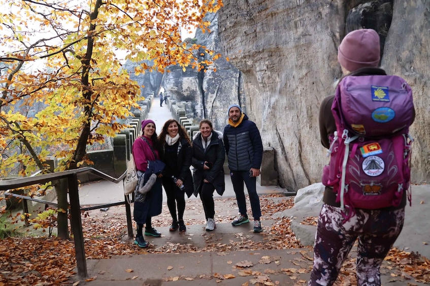 A group of people standing on a stone pathway surrounded by autumn leaves and a rocky cliff. 1