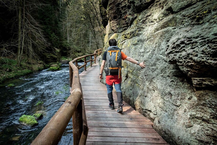 A person hiking on a wooden bridge over a river, surrounded by forested cliffs. 5