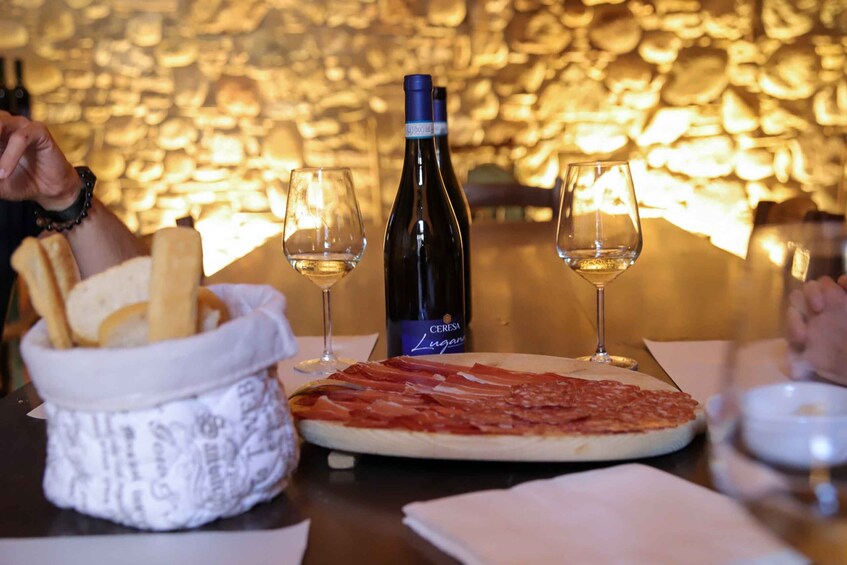 Une table avec une pizza, une bouteille de vin, des verres et un panier de gressins. 2