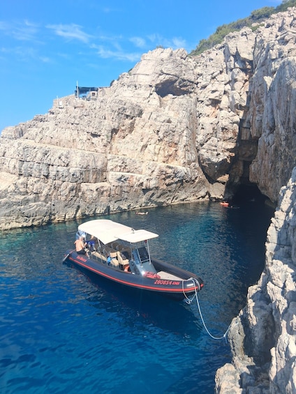 A boat anchored near rocky cliffs with clear blue water. 2