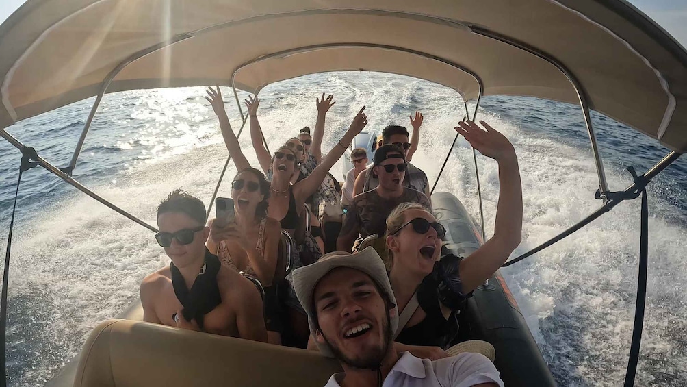 A group of people on a boat with their hands raised, enjoying the sea. 4