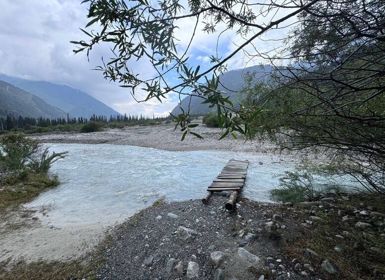 A river with a wooden bridge, surrounded by mountains and trees. 1