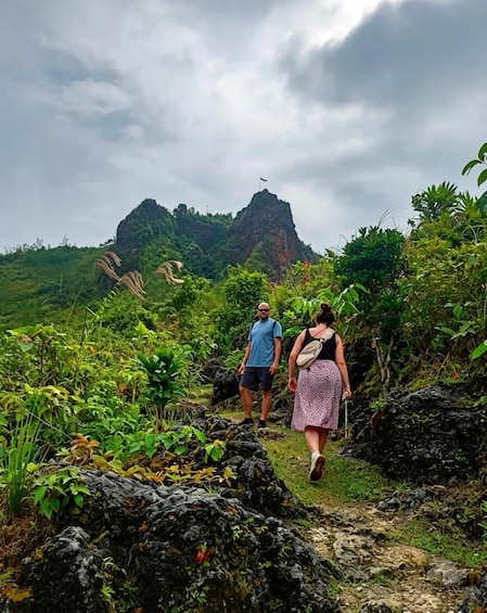 Two people hiking on a rocky trail with lush greenery and a mountain in the background. 4