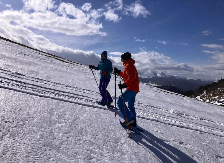 Two skiers on a snowy slope with a clear sky and distant mountains. 1