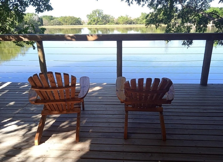 Two wooden Adirondack chairs on a wooden deck overlooking a calm lake. 3