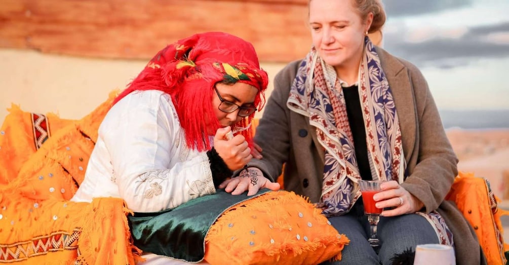 Two people sitting on a camel, one holding a drink. 1