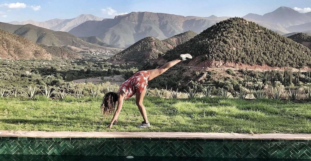 A person performing a yoga pose on grass with mountains in the background. 5