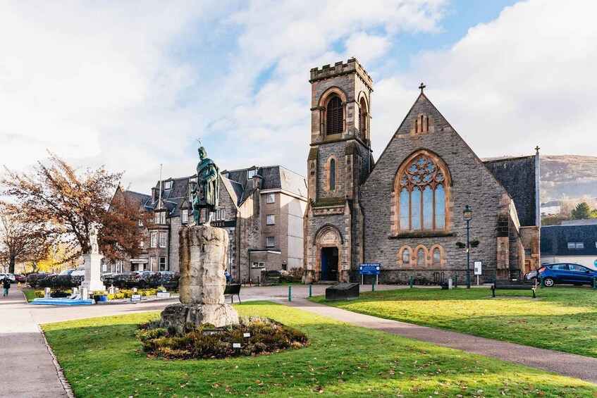 A historic church with a tall tower and a large arched window, surrounded by a grassy area and a statue. 5
