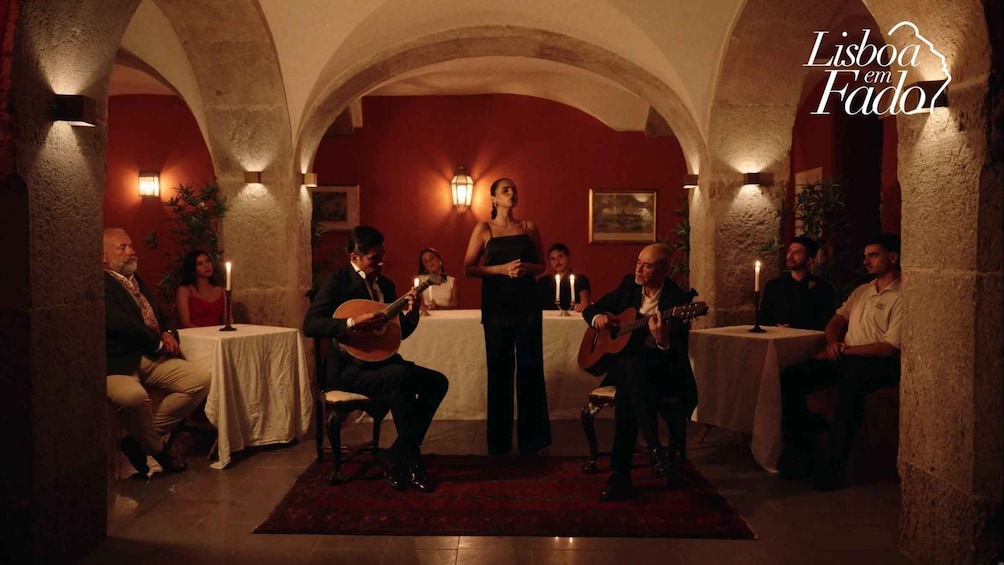 A group of people in a dimly lit room with stone arches, a woman singing, and two guitarists. 1