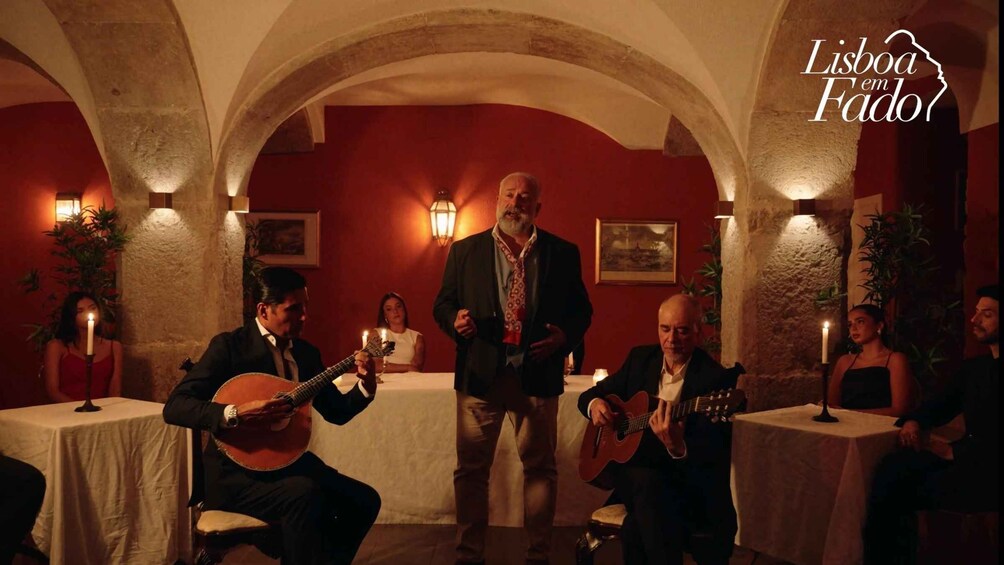 A group of people playing guitars in a warmly lit room with red walls and stone arches. 3