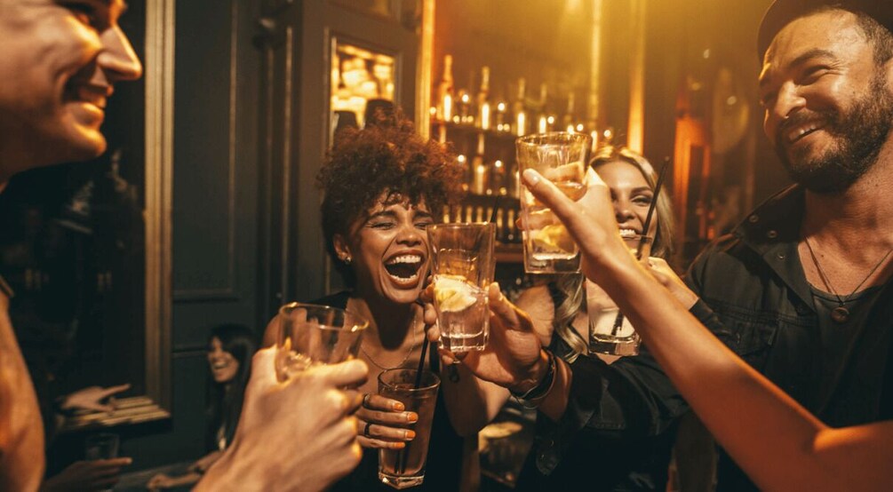 A group of people toasting with drinks in a dimly lit bar. 4