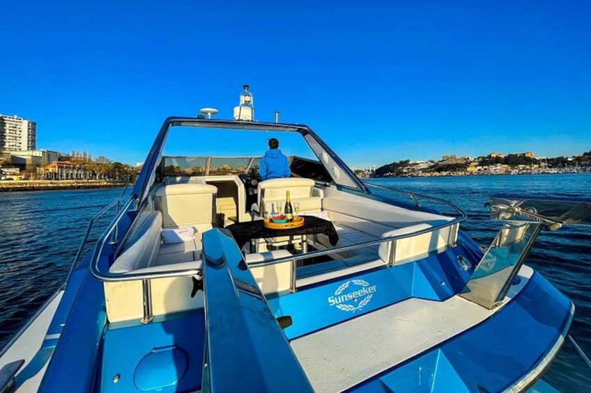 Un velero azul con una persona al timón, amarrado en aguas tranquilas bajo un cielo despejado y una costa lejana. 3