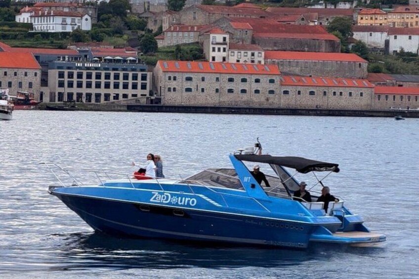 Un velero azul con la inscripción 'Zad Euro' en el costado, navegando sobre aguas tranquilas con un paisaje urbano al fondo. 5