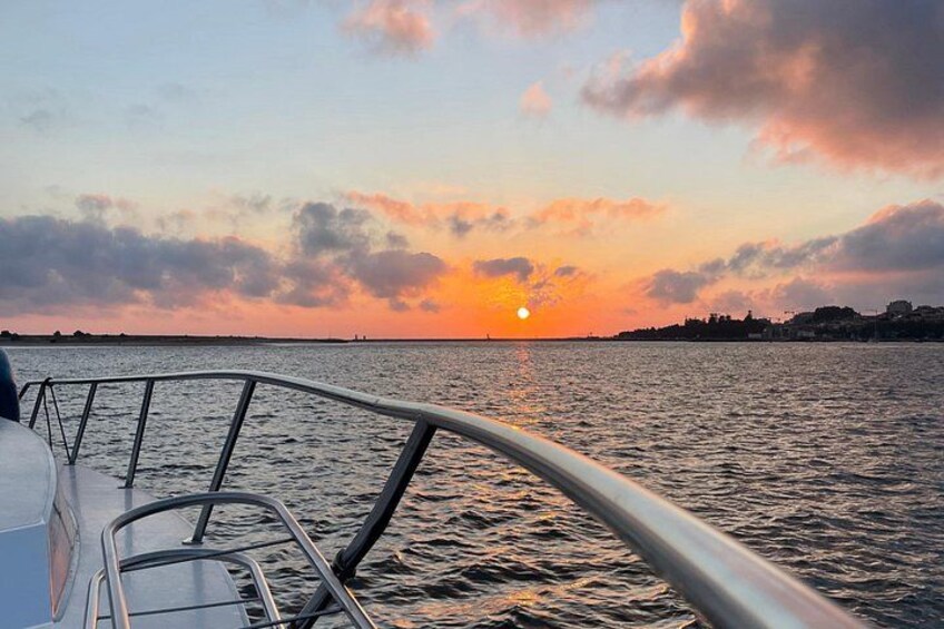 Solnedgang over vand med gelænder fra en båd i forgrunden. 3