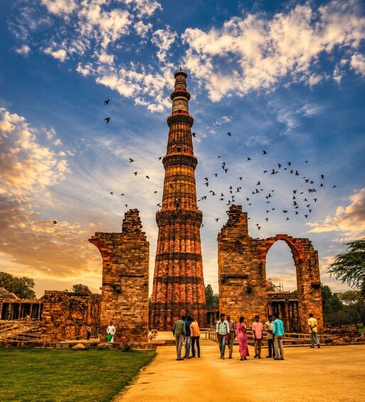 A historical tower with intricate architecture, surrounded by ruins and a clear sky with birds flying. 3