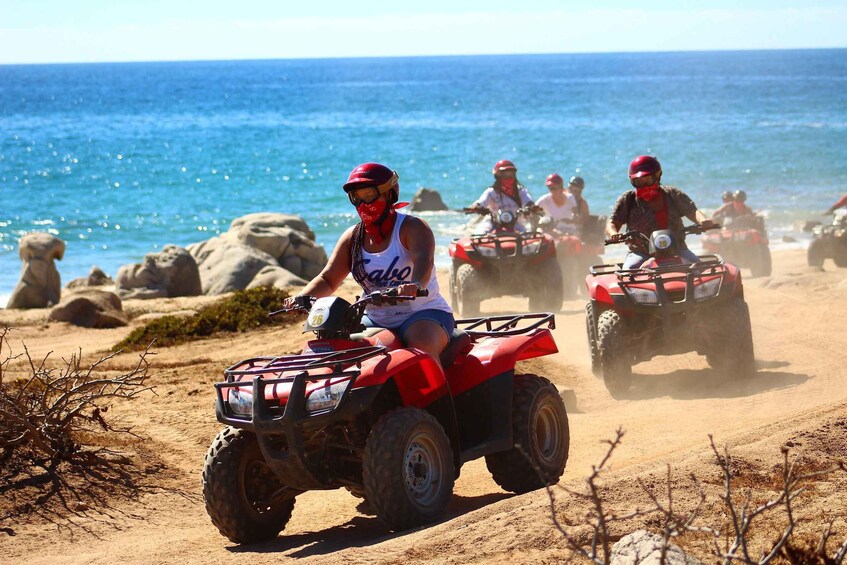 People riding ATVs on a sandy beach with the ocean in the background. 1