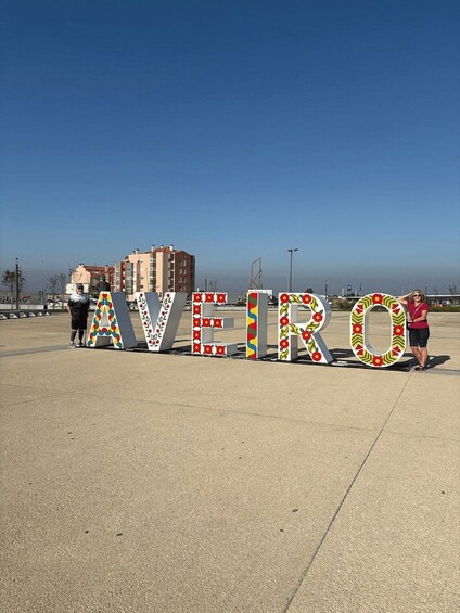 Store, farverige bogstaver der staver 'AVEIRO' på en betonoverflade med bygninger i baggrunden. 4