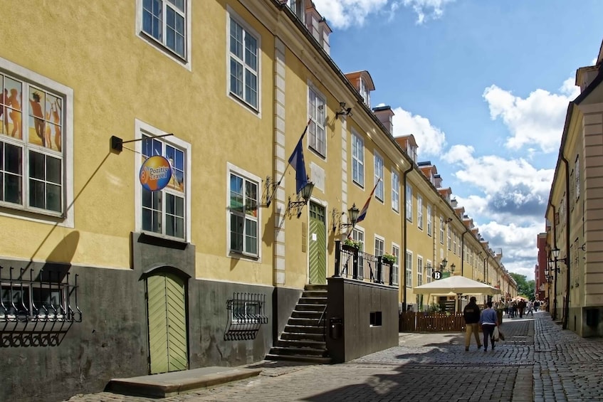 A cobblestone street lined with yellow buildings, a green gate, and a sign for Positiv Travel. 4