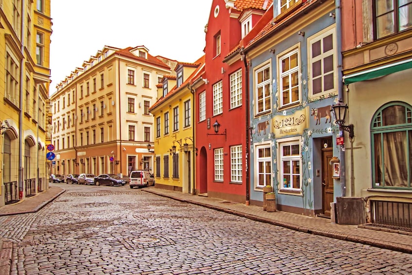 A cobblestone street lined with colorful buildings, including a restaurant named "Restorans." 1