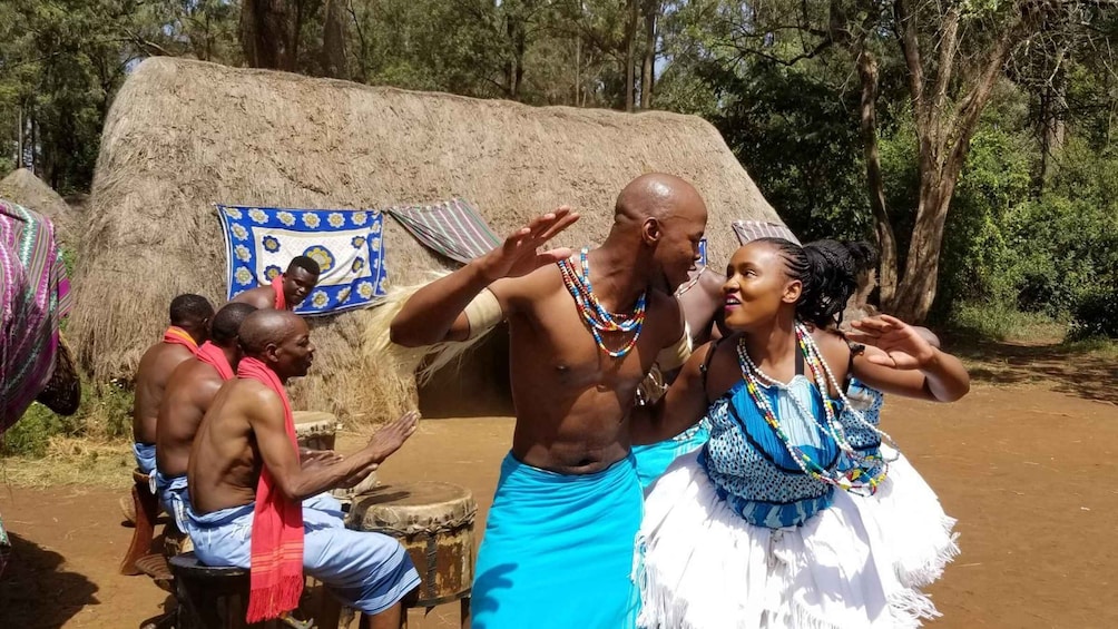 A group of people in traditional attire performing a dance in front of a thatched structure. 2