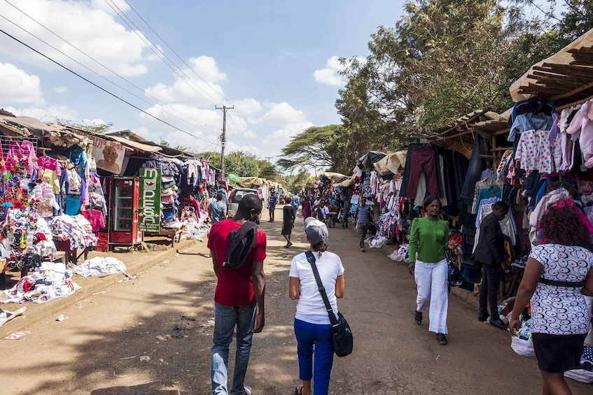 A bustling outdoor market with various stalls selling clothes and household items. 1
