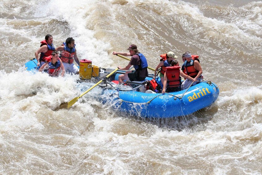 A group of people in a blue raft navigating through rough, fast-moving water. 3